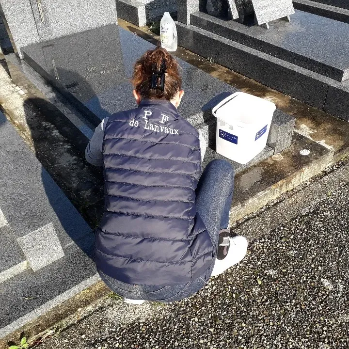 Nettoyage manuel d'un monument funéraire en granit par une professionnelle au cimetière.