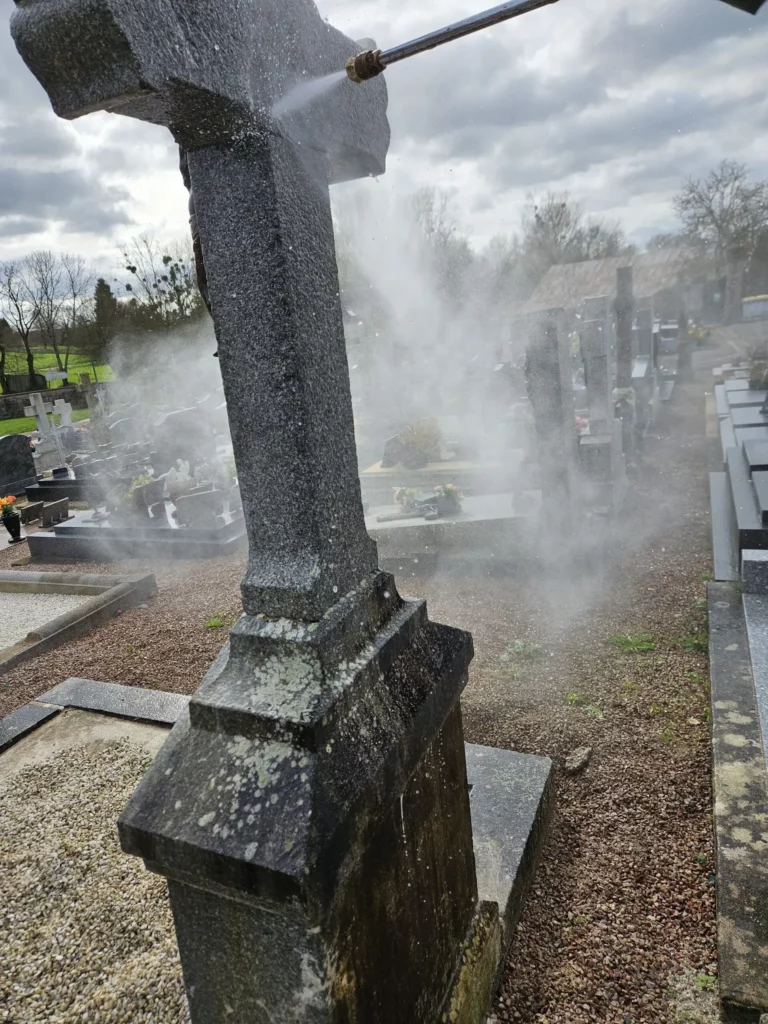 Décapage haute pression à l'eau d'une vieille croix tombale en pierre dans un cimetière.