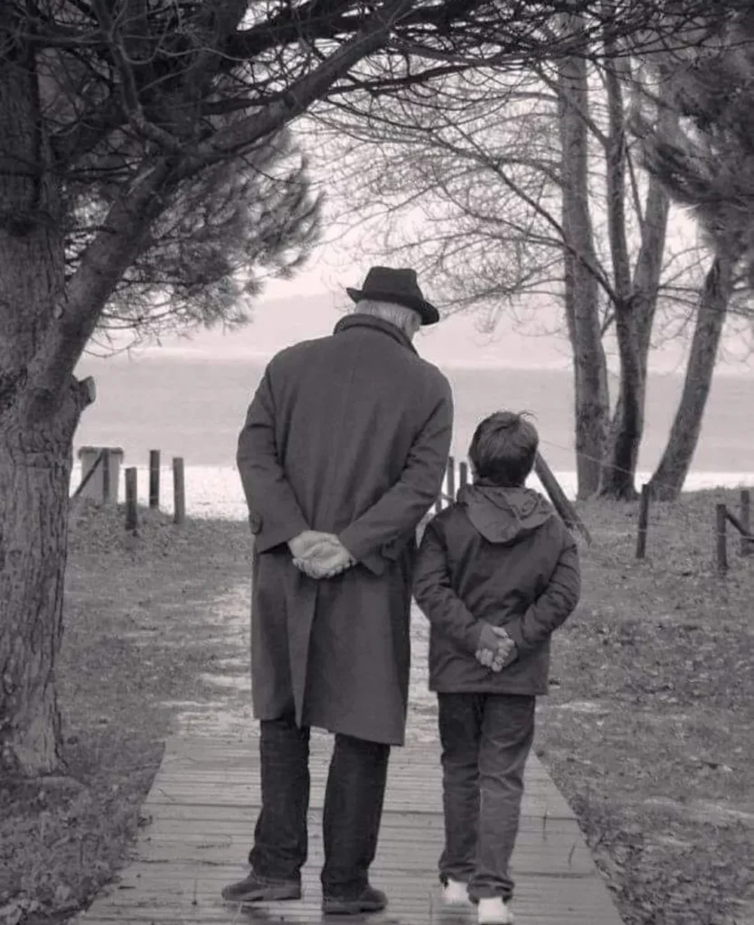 Homme et enfant de dos marchant vers la mer sur un ponton de bois.