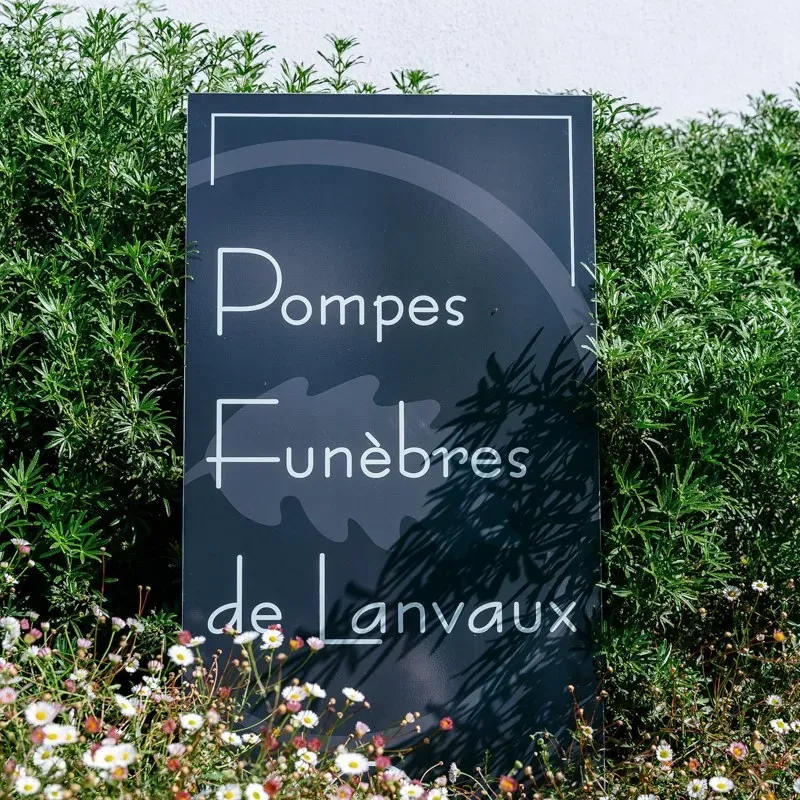 Enseigne de Pompes Funèbres de Lanvaux entourée de fleurs et verdure.